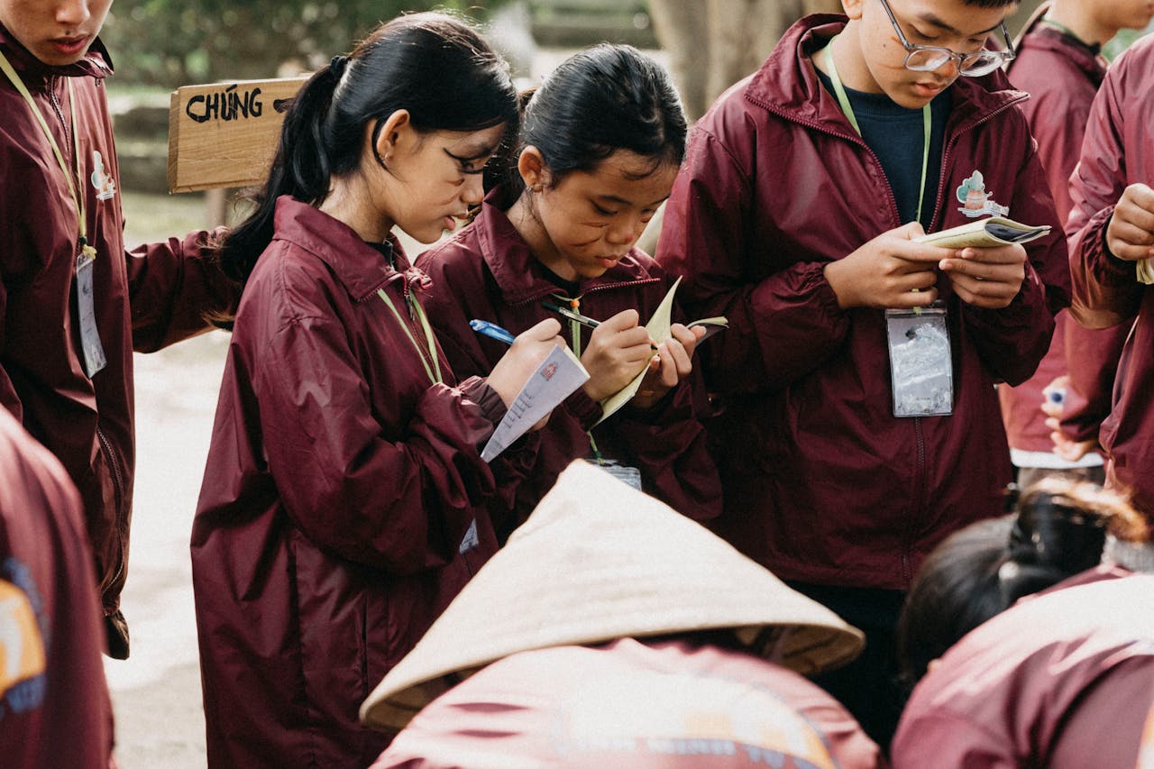 A group of students wearing burgundy jackets taking notes during an outdoor educational event.